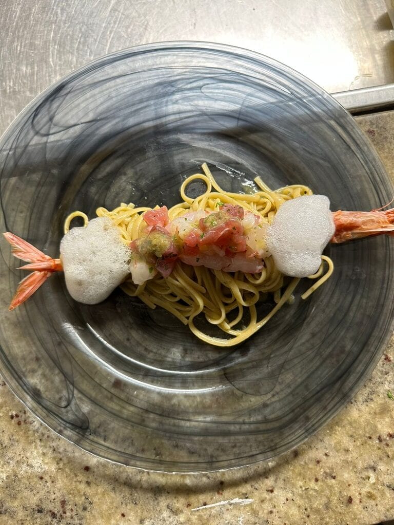 Pasta dish with shrimp and foam on transparent plate.