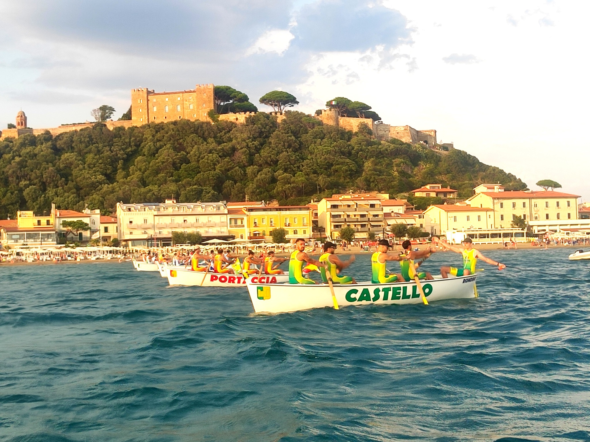 Palio di Castiglione della Pescaia: equipaggi in gara con il castello sullo sfondo.